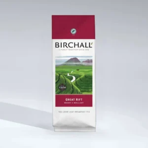 A bag of Birchall Great Rift Loose Tea with a vibrant red top showcases packaging ideal for a café atmosphere. It features an illustration of a lush green landscape, complete with a winding river and distant mountain, accompanied by the text: "A family tradition since 1872.