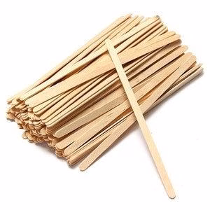 A collection of Wooden Stirrers 1000 x 5.5 inch or 1000 x 7 inch, reminiscent of those used by a barista in a cozy café, is scattered about. One stirrer lies separately on top. The stirrers are light brown and uniformly shaped, perfect for crafts or stirring.