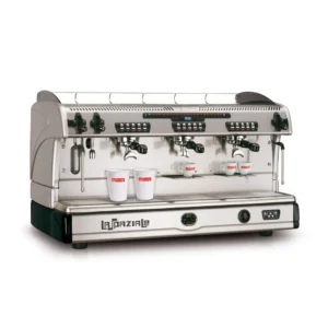 The La Spaziale S5 EK Automatic Takeaway 3 Group Espresso Coffee Machine, with its polished stainless steel finish, is an ideal addition to any café. This machine is a barista's delight, offering three group heads, steam wands for frothing milk, and a variety of control buttons. On the drip tray sit two white cups marked with a red logo, accompanied by decorative cup rails on top.