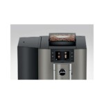The Jura X10 Dark Inox - Tanked Bean to Cup Coffee Machine boasts a sleek silver and black design with a digital display and user-friendly buttons on the front. Its sophisticated barista-style touch is complemented by the visible coffee beans behind a clear cover on top.